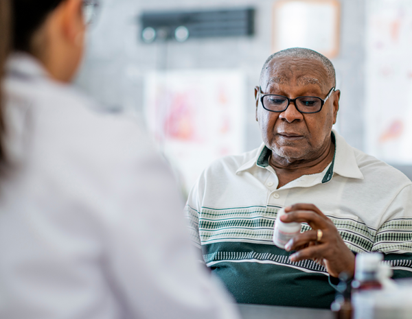 Older man examining a pill bottle with a pharmacist