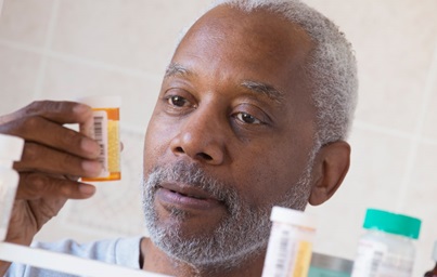 Man looking at pill bottle in bathroom mirror